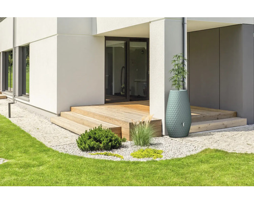 Dekorativer Regenspeicher und Pflanzkübel an einer Holzterrasse eines modernen Wohnhauses mit Garten und Rasenfläche.