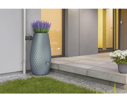 Moderner grauer Regenspeicher mit Rautenmuster und integrierter Pflanzschale mit Lavendel an einer Hauswand neben einem Fallrohr.