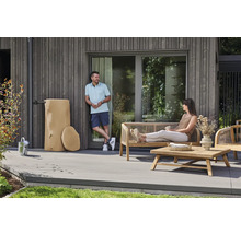 Regenspeicher in Baumstamm-Optik neben Gartenmöbeln aus Holz auf einer modernen Terrasse mit grauen Dielen.
