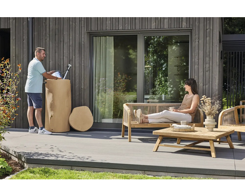 Moderner Außenbereich mit einer Holzterrasse, Gartenmöbeln aus Holz und einem dekorativen Regenwasserbehälter in Baumstamm-Optik.