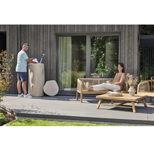Ein Mann befüllt eine Gießkanne an einer Regentonne in Baumstammoptik auf einer modernen Terrasse mit Gartenmöbeln aus Holz.