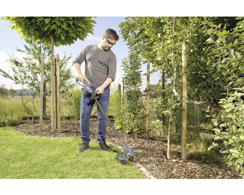 Ein Mann benutzt einen Rasentrimmer im Garten, um Rasen zu schneiden.