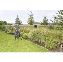 Ein Mann trimmt mit einem Rasentrimmer den Rasen in einem Garten.