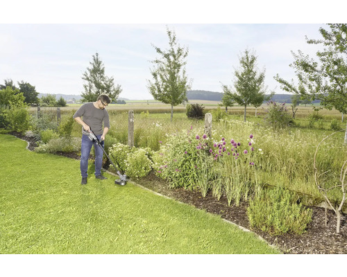 Ein Mann trimmt mit einem Rasentrimmer den Rasen in einem Garten.