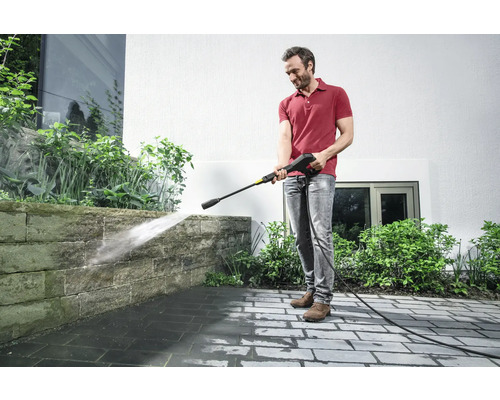 Mann reinigt Steinmauer mit einem Hochdruckreiniger im Außenbereich.