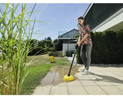 Frau reinigt Terrasse mit Flächenreiniger und Hochdruckreiniger im Garten.