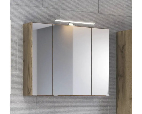 Dreitüriger Spiegelschrank im Holzdesign mit LED-Aufsatzleuchte montiert an einer grauen Fliesenwand.