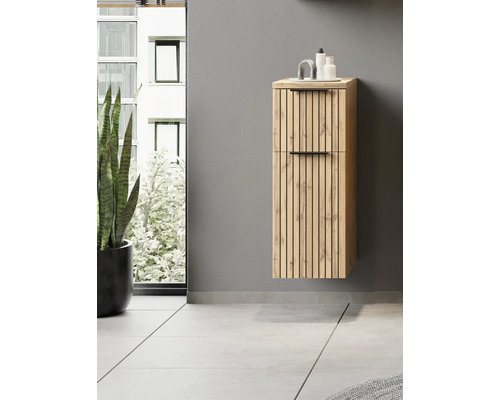 Wandhängender Bad-Hochschrank in Eichenoptik mit schwarzen Leisten und Griffen in einem modernen, hellen Badezimmer neben einer Pflanze.
