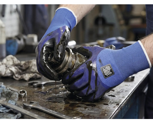 Eine Person hält eine ölige mechanische Komponente mit Arbeitshandschuhen.