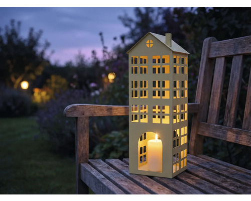 Windlicht in Hausform mit Kerze auf einer Holzbank im Garten