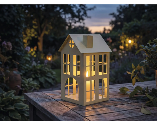 Windlicht in Hausform mit Kerze auf Holztisch im Garten