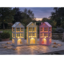 Drei dekorative Hauslaternen auf einem Holztisch im Freien.