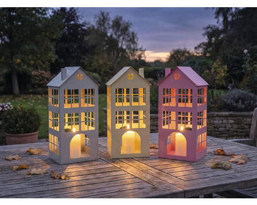 Drei dekorative Hauslaternen auf einem Holztisch im Freien.