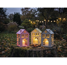 Drei Hauslaternen mit Kerzen auf einem Baumstumpf im Garten