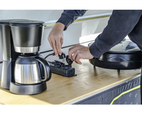 Eine Person schliesst eine Kaffeemaschine an eine Mehrfachsteckdose an.