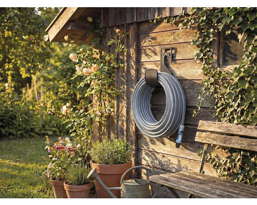 Gartenszene mit Schlauchaufroller an Holzwand, umrankt von Pflanzen