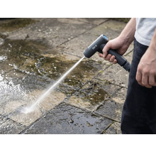 Eine Person reinigt mit einem Akku-Hochdruckreiniger Steinplatten im Außenbereich.
