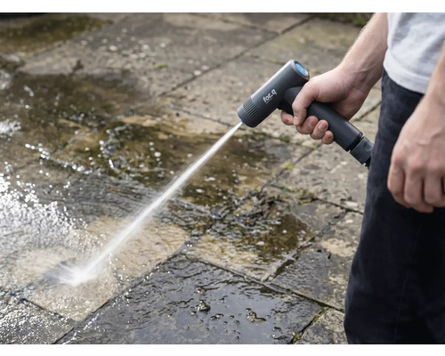 Eine Person reinigt mit einem Akku-Hochdruckreiniger Steinplatten im Außenbereich.