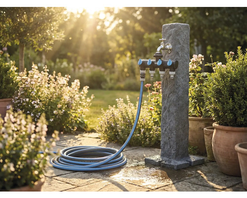 Gartenszene mit Wasserzapfsäule, Mehrfachverteiler und Gartenschlauch auf Steinterrasse