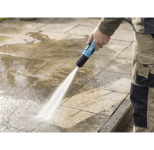 Eine Person reinigt eine Steinterrasse mit einem for_q-Gartenschlauch