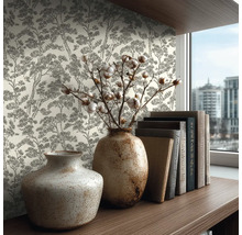 Vliestapete mit Baum-Muster im Skizzenstil an einer Wand hinter einem Holzregal mit Keramikvasen und Büchern in einem hellen Zimmer.