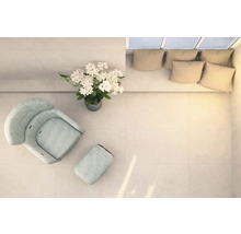 Helle Räumlichkeit mit Sessel, Fußhocker, Blumenarrangement und Couch mit Kissen, von oben aufgenommen