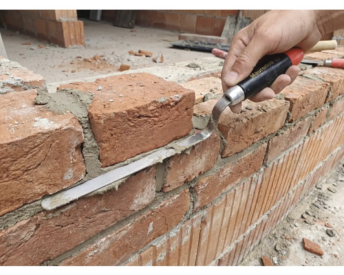 Handwerker bearbeitet Ziegelwand mit Fugenkelle