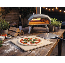 Außenaufnahme eines Ooni Pizzaofens mit Pizza, Pizzaschieber und Zutaten auf einem Holztisch.