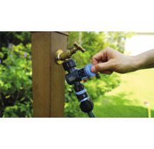 Gartenwasserhahn mit Wasserverteiler und angeschlossenem Gartenschlauch in der Anwendung.