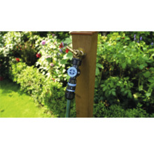 Gartenszene mit Wasserhahn an Holzpfosten und angeschlossenem Gartenschlauch