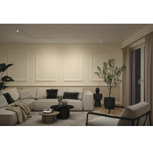 Modernes Wohnzimmer mit hellem Ecksofa, runden Couchtischen, Zierprofilen an der Wand und einem Schienensystem für die Deckenbeleuchtung.