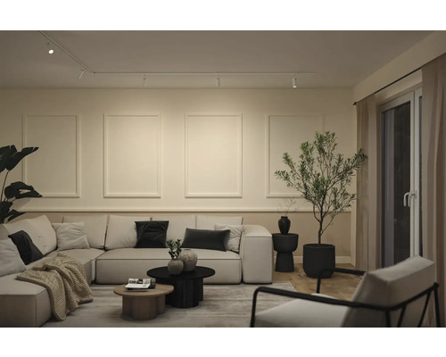 Modernes Wohnzimmer mit hellem Ecksofa, runden Couchtischen, Zierprofilen an der Wand und einem Schienensystem für die Deckenbeleuchtung.
