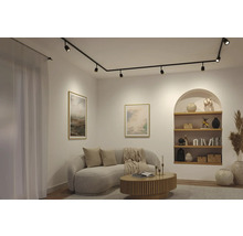 Modernes Wohnzimmer mit schwarzem Schienensystem an der Decke, geschwungenem Sofa und hölzernem Couchtisch vor hellen Wänden.