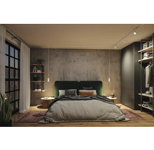 Modernes Schlafzimmer mit Doppelbett, dunkelgrünem Kopfteil, Wandpaneelen in Betonoptik, weißen Pendelleuchten, Schienensystem und Kleiderschrank.