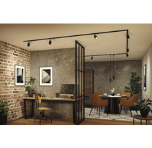 Moderner Wohnbereich mit Heimbüro und Esszimmer, getrennt durch eine Glastrennwand. Schwarzes Schienensystem an der Decke, Ziegel- und Betonwände.
