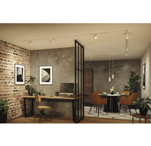 Modernes Industrie-Interieur mit weißem Schienensystem an der Decke, das Arbeitsplatz und Essbereich vor Beton- und Ziegelwänden beleuchtet.