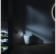 Modernes Badezimmer mit wandhängender Toilette, integrierter Betätigungsplatte und nächtlichem Stadtblick durch ein großes Fenster.