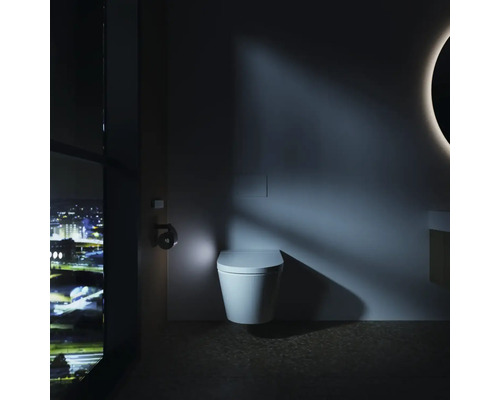 Modernes Badezimmer mit wandhängender Toilette, integrierter Betätigungsplatte und nächtlichem Stadtblick durch ein großes Fenster.