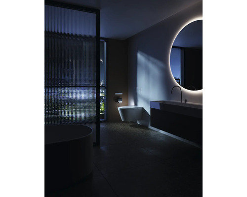Modernes, dunkel gestaltetes Badezimmer mit beleuchtetem Rundspiegel, wandhängendem WC, Waschplatz und strukturierter Glastrennwand.