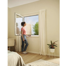 Frau am offenen Fenster mit Insektenschutzgitter im Schlafzimmer