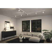 Modernes Wohnzimmer mit weißem Schienensystem an der Decke, grauem Sofa, schwarzen Fenstern und einem Sideboard.