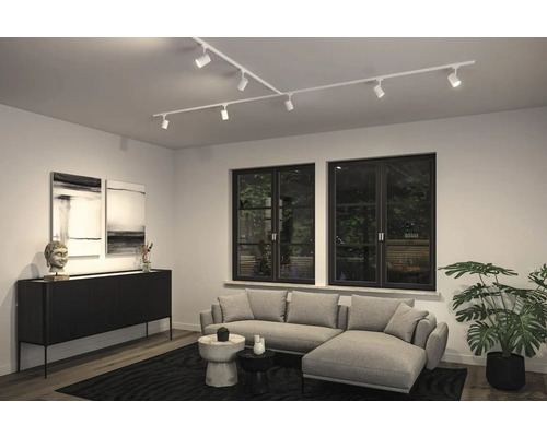 Modernes Wohnzimmer mit weißem Schienensystem an der Decke, grauem Sofa, schwarzen Fenstern und einem Sideboard.