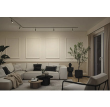 Modernes Wohnzimmer mit hellem Ecksofa, Schienensystem mit Spots an der Decke und dekorativer Wandgestaltung mit Rahmenleisten.
