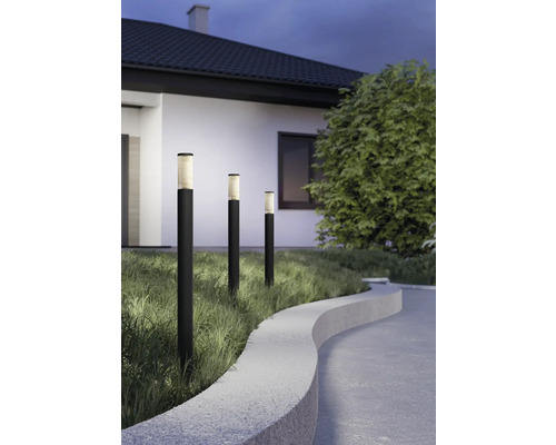 Drei moderne schwarze Wegeleuchten in einem Garten neben einem gepflasterten Weg mit Steineinfassung und Gras bei Dämmerung.