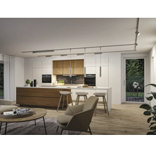 Moderne Küche mit Holzinsel, weißen Schränken und Schienensystem an der Decke. Heller Wohnbereich mit Sessel, Couchtisch und Holzfußboden.