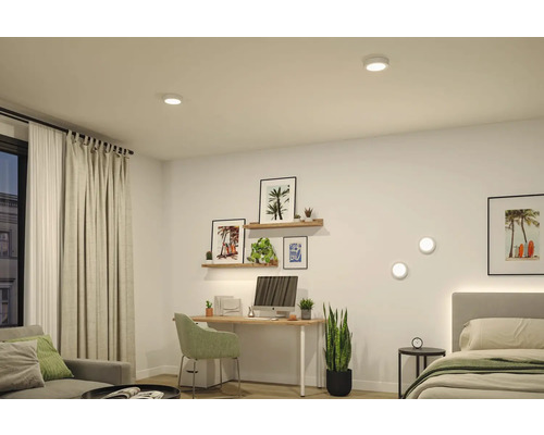 Hell eingerichtetes Zimmer mit Schreibtisch und Bett sowie runden Decken- und Wandleuchten.