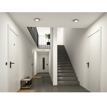 Moderner, heller Flur mit weißen Türen, schwarzen Türgriffen und einer grauen Betontreppe. Deckenspots beleuchten den Raum mit dunklem Boden.