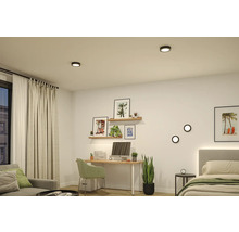 Modernes Zimmer mit Schreibtisch, Bett und Sofa, beleuchtet durch runde schwarze LED-Decken- und Wandleuchten. Helle, organisierte Einrichtung.