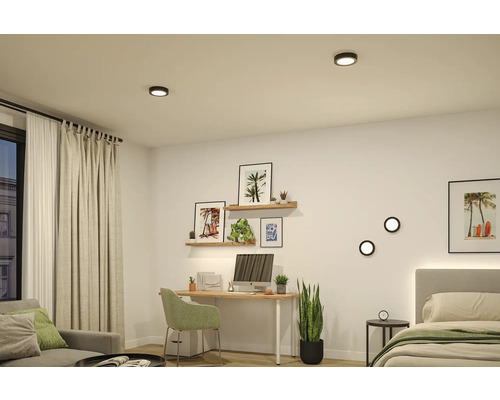 Modernes Zimmer mit Schreibtisch, Bett und Sofa, beleuchtet durch runde schwarze LED-Decken- und Wandleuchten. Helle, organisierte Einrichtung.