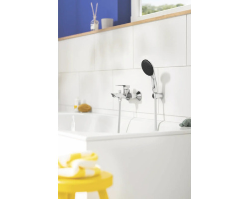 Moderne Badewannenarmatur in Chrom-Optik mit Handbrause an einer weiß gefliesten Wand in einem hellen Badezimmer.